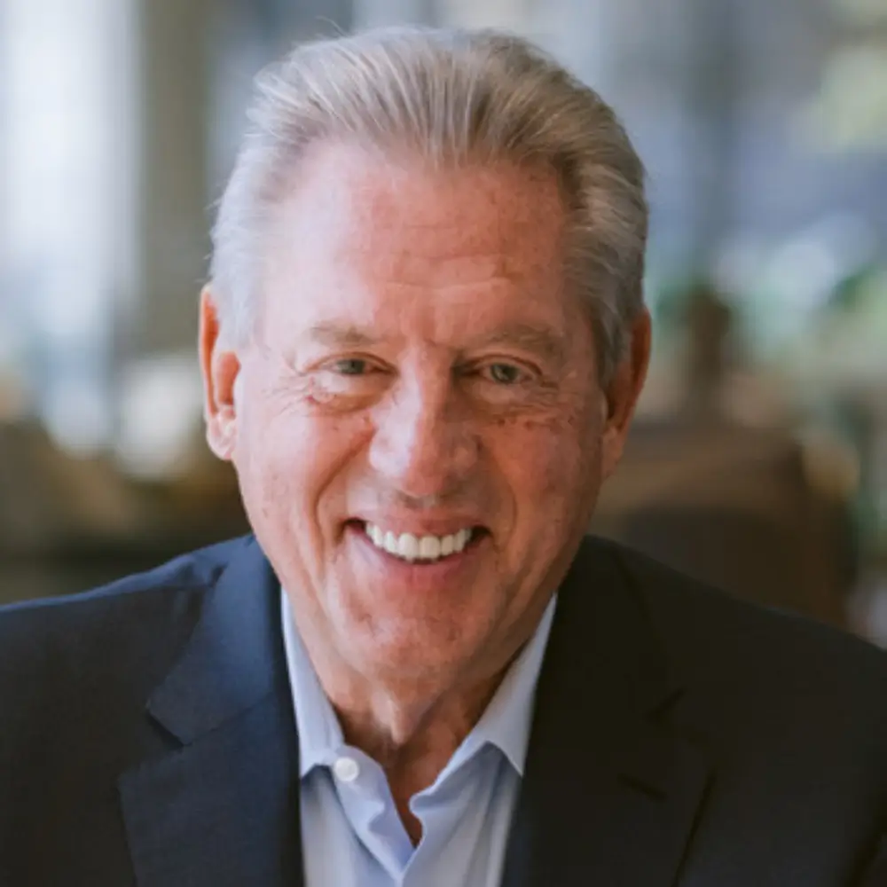 Smiling older man in a suit jacket with a blurred background.