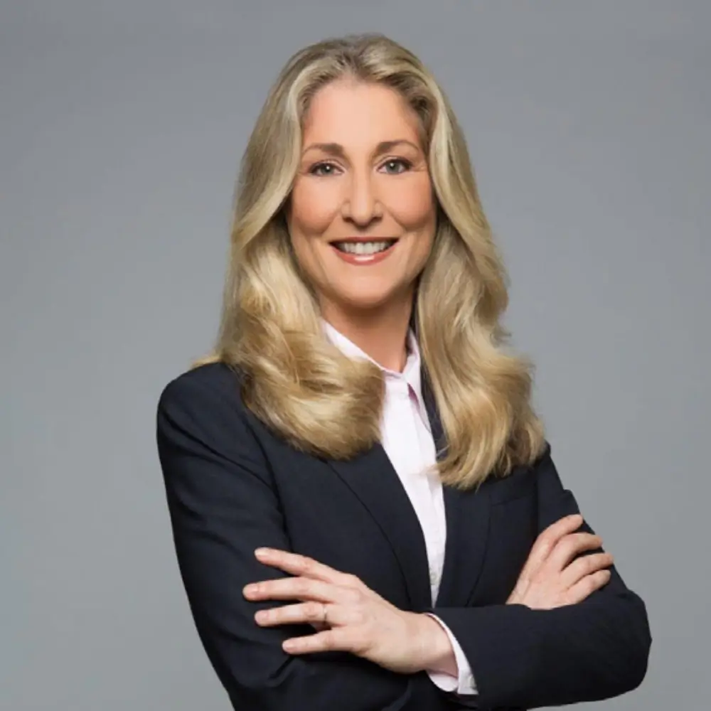 Professional woman with long blonde hair in business attire smiling confidently.